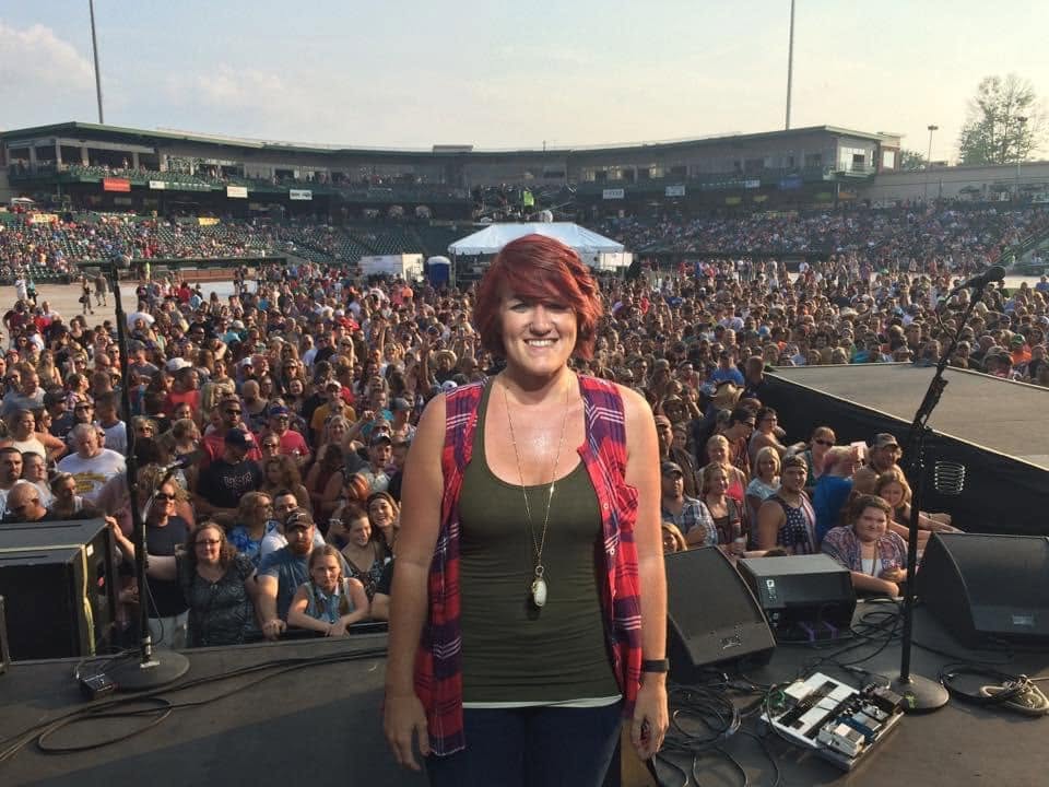 Staci smiling onstage in front of a large outdoor audience